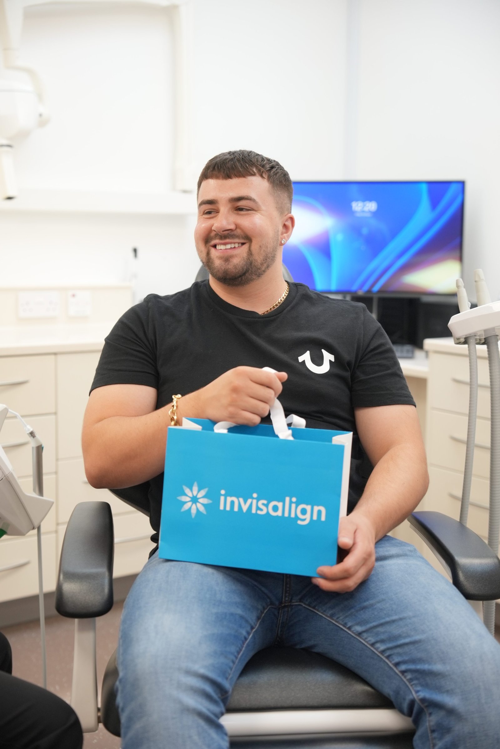 Invisalign patient sitting in dentist chair holding Invisalign bag